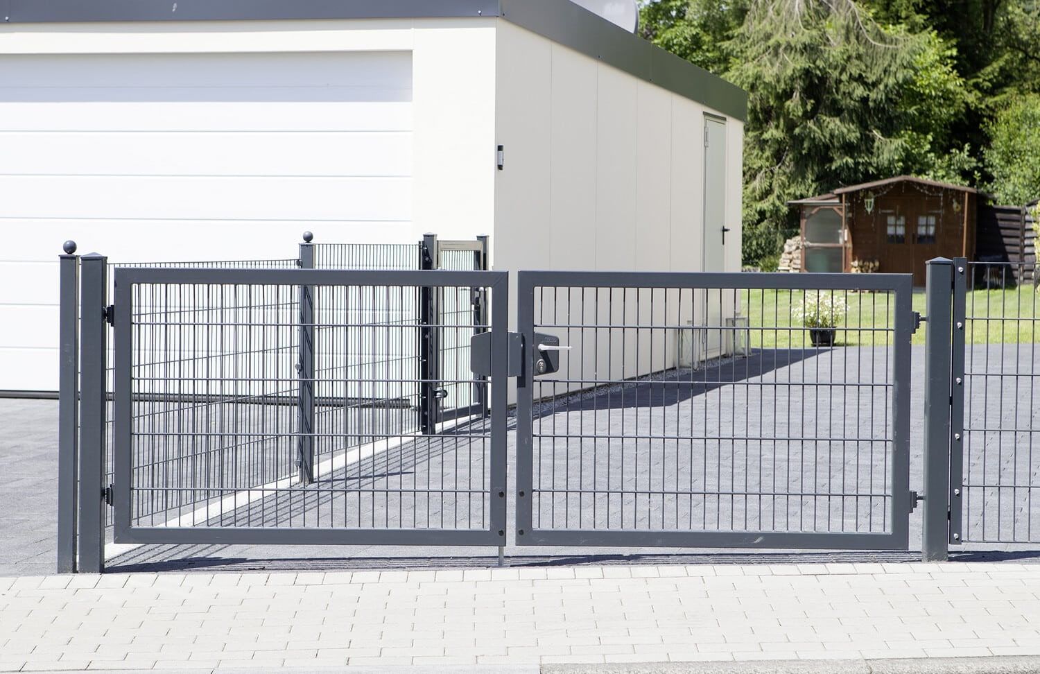 Zweiflügeliges Gartentor in Anthrazit vor einer gepflasterten Garageneinfahrt