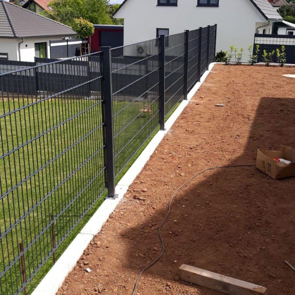 Anthrazitfarbener Doppelstabmattenzaun auf durchlaufendem Betonstreifen, Erdreich daneben noch offen